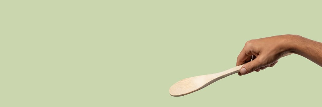 Black male hand holding a wooden cooking spoon isolated on light green background. High quality photo