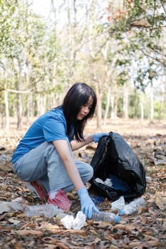 young woman holds a garbage bag and a group of Asian volunteers collect garbage in plastic bags and clean up