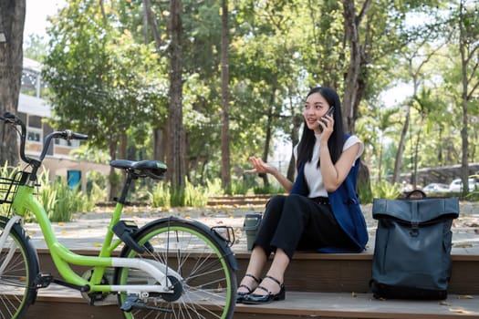 Asian business woman sitting and working in a nature park Travel by bicycle to save the environment.