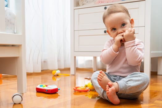 The baby plays with toys while sitting on the parquet floor.