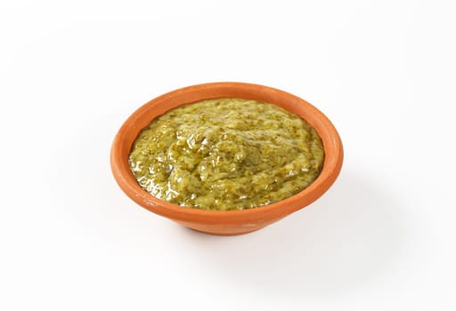 Basil pesto in terracotta bowl on white background