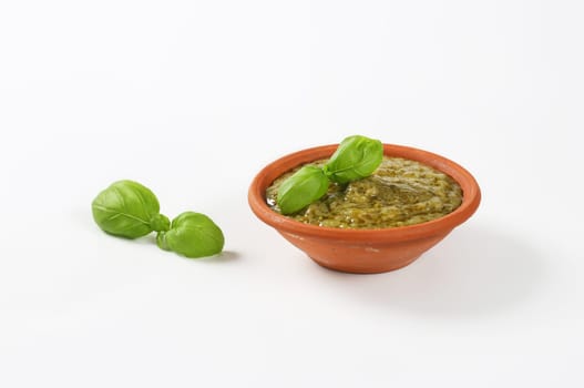 Basil pesto in terracotta bowl on white background