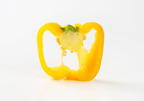 Slice of yellow bell pepper (cross section) on white background