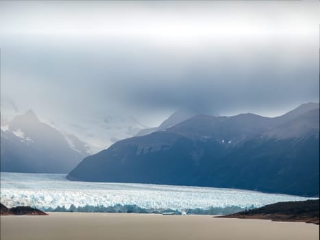 Glacier and mountains under dramatic cloudy sky.
