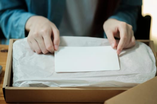 Person preparing a package with a blank card for a custom message. Product packaging and personalization concept. Design for e-commerce, gift wrapping services.