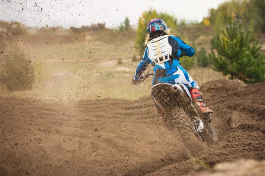 Moto cross - MX girl biker at race in Russia - a sharp turn and the spray of dirt, rear view, telephoto