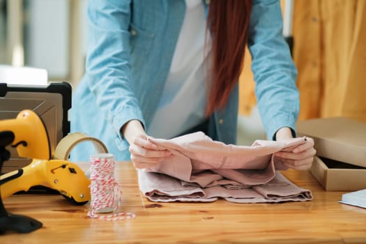 Smiling female entrepreneur packing clothing items for shipping in her startup workshop.