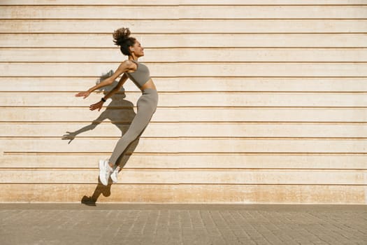 Young fit woman in sportswear leaping in the air with wall backdrop outdoors. High quality photo