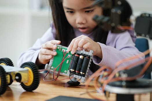 Asian girl concentrating on building a robot, embodying STEM education.