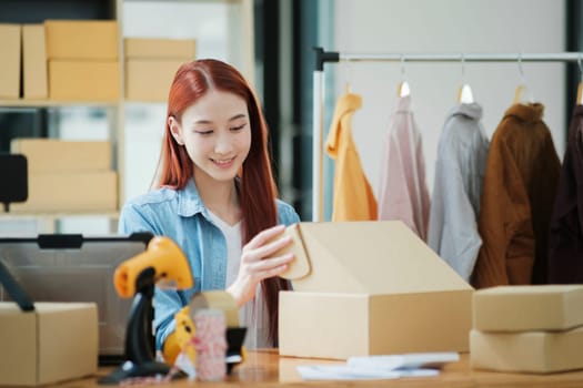 Smiling female entrepreneur packing clothing items for shipping in her startup workshop.