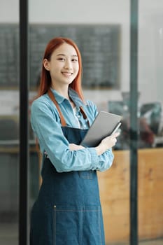 Smiling female entrepreneur with digital tablet in coffee shop. Small business and hospitality concept. Young cafe owner managing orders.