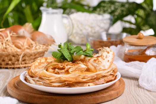 Homemade thin crepe (pancakes) with honey stacked in a stack, on a table with milk and eggs in a basket. Country style food. Traditional Slavonian, pagan holiday Maslenitsa