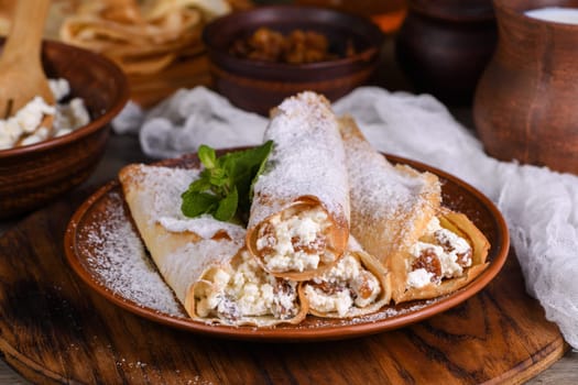 Thin pancakes filled with cottage cheese, honey and raisins, rolled in the form of a tube, sprinkled with powdered sugar, garnished with mint. Festive dish for the pagan Slavic holiday Maslenitsa