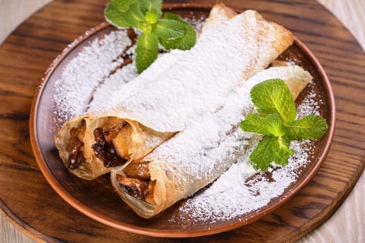 Homemade thin pancakes. The apples are cooked in a buttery caramel sauce with raisins and cinnamon and stuffed into a thin pancake. Garnish with powdered sugar and mint. Food in a rustic style.