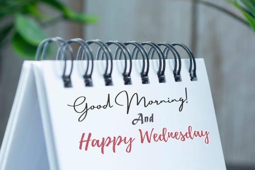 Good morning and happy wednesday text on white calendar with potted plant background on wooden desk.