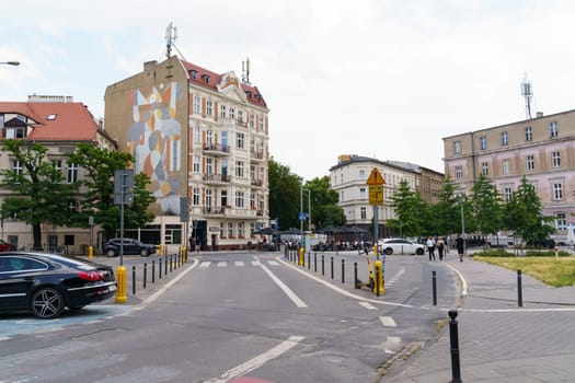 Poznan, Poland - June 18, 2023: Pedestrians cross the road and cars pass through an urban European intersection in Poznan on a clear spring day against the backdrop of historic architecture.