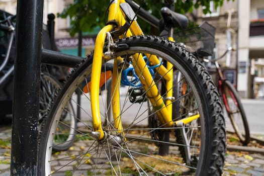 A vibrant yellow bicycle is parked neatly next to a black pole in an urban setting.