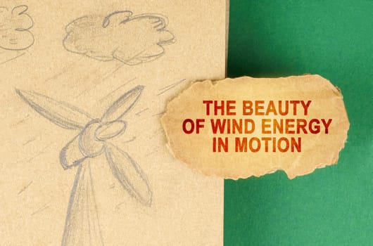 Alternative energy concept. On a green surface there is a drawing with a wind generator and a cardboard with the inscription - The beauty of wind energy in motion