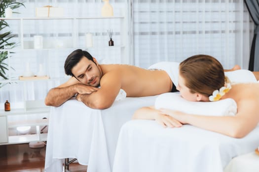 Blissful couple customer having exfoliation treatment in luxury spa salon with warmth candle light ambient. Salt scrub beauty treatment in health spa body scrub. Quiescent