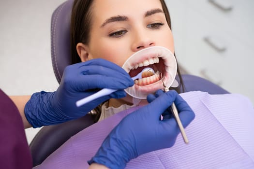 Portrait of young woman in dental clinic. Dentist in rubber gloves doing check up