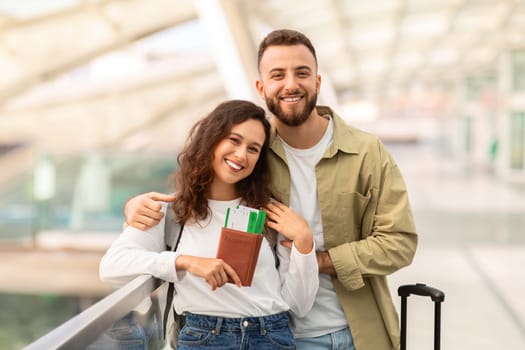 Travel Advertisement. Happy Young European Couple Posing At Airport, Cheerful Millennial Spouses Smiling At Camera While Waiting Flight At Terminal, Woman Holding Passports With Tickets, Copy Space