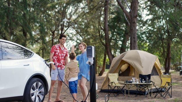 Outdoor adventure and family vacation camping in nature travel by eco friendly car for sustainable future. Lovely family recharge EV car with EV charging station in campsite. Perpetual