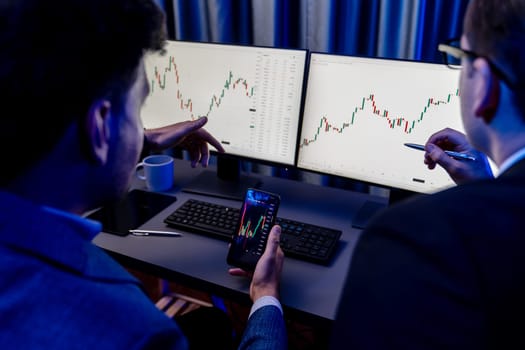 Two stock exchange traders researching data on smartphone and laptop screen server of dynamic digital currency. Investors analyzing market stock at decorative neon blue-light of workplace. Sellable.