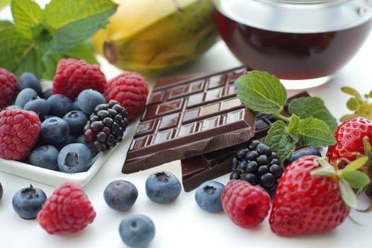 Assorted berries and dark chocolate on a white plate. Close-up food photography. Healthy eating and dessert concept. Design for recipe, food blog, culinary arts, and nutrition guide