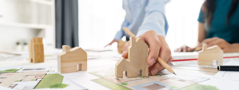 Professional architect engineer team discussion about architectural project on meeting table with wooden block and blueprint scatter around. Design and cooperate concept. Closeup. Delineation.