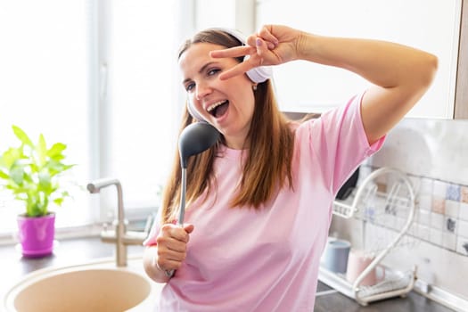 Joyful young woman pretending to sing into a ladle while cooking in a bright kitchen.