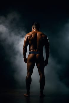 A lone figure of a man wearing only underwear standing in a dimly lit room.