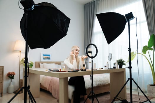 Young woman making beauty and cosmetic tutorial video content for social media. Beauty blogger smiles to camera while showing how to apply beauty skincare to audience or followers. Blithe