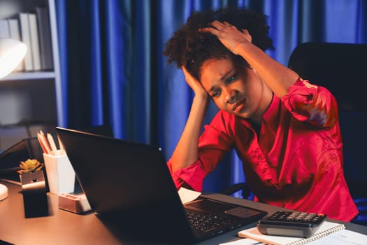 African woman businesswoman, wearing pink shirt having headache with migraine, sitting at computer laptop with leaning position. Concept of work form home with pressure and tension. Tastemaker.