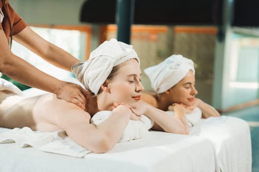 Couple of beautiful young woman lie on white spa bed during having back massage. Attractive caucasian woman having back massage at traditional spa room. Relaxing and healthy concept Tranquility.