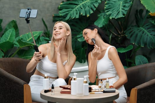 Two beautiful content creator making natural beauty and cosmetic tutorial on green plant garden video. Beauty blogger showing how to beauty care to social medial audience using selfie stick . Blithe