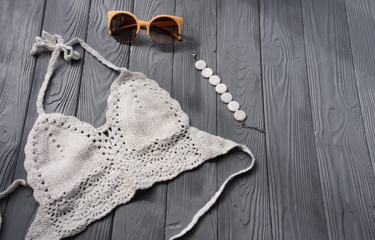 white knitted top woman trending two-piece swimsuit beach swimwear fashion sunglasses. Summer background template mockup space pattern composition sample text. Top view above grey wooden background.