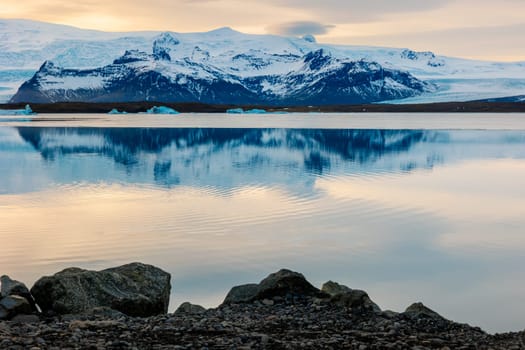Icy scandinavian big lake in iceland, snowy mountain tops and hills in arctic northern landscape. Beautiful sunset golden hour near frosty natural highland, winter wonderland scenic route.
