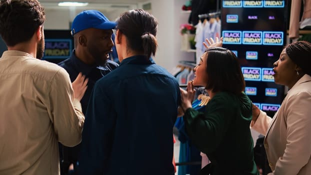 Security officer calms crowd on black friday sales rush, pushing people back and trying to control clothing store entrance. Clients shoppers being impatient, obsessed with cheap prices.