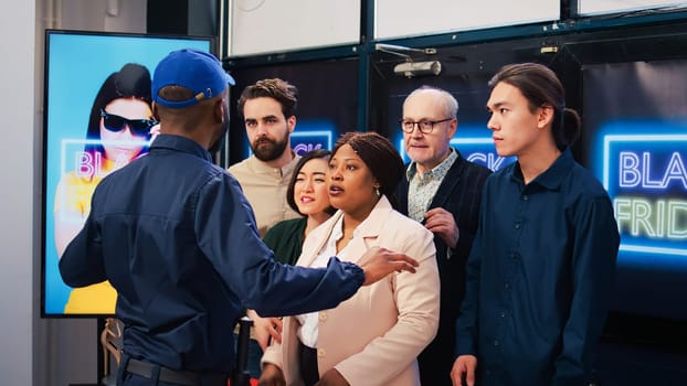 Impatient group of customers fighting with retail store employee, pushing man to enter first in fashion outlet. Angry eager shoppers going crazy during black friday sales event.