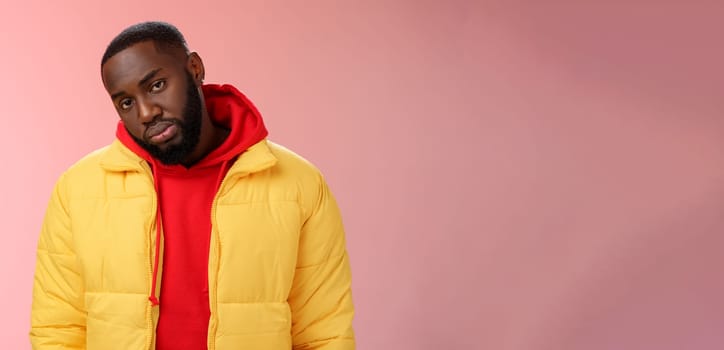 Unimpressed bored ignorant young african bearded man tilt head look scorn uninterest camera listen boring useless information, standing careless in yellow jacket red hoodie, indifferent.