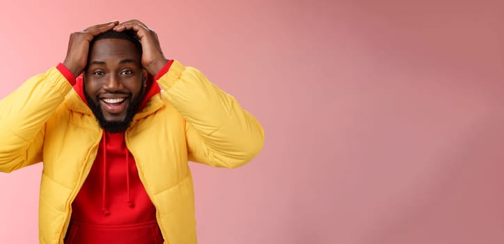 Waist-up surprised happy lucky young african-american bearded male in yellow jacket holding hands head smiling impressed joyfully receive awesome proposal dream come true, pink background.