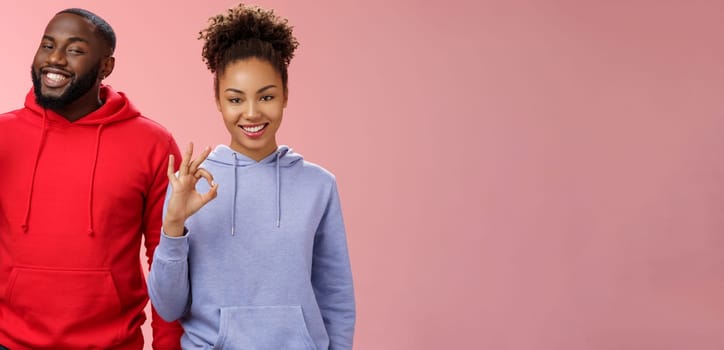 Two african-american skilful coworkers professionals assured friend everything perfect smiling broadly delighted nodding agree approval gesture show okay ok not bad choice sign, pink background.