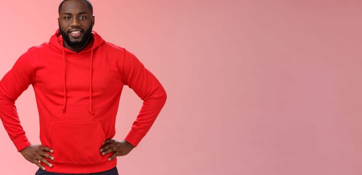 Helpful attractive friendly bearded african-american boyfriend wearing red hoodie hold hands waist smiling wanna help asking what do, lending hand, standing confident assertive pink background.