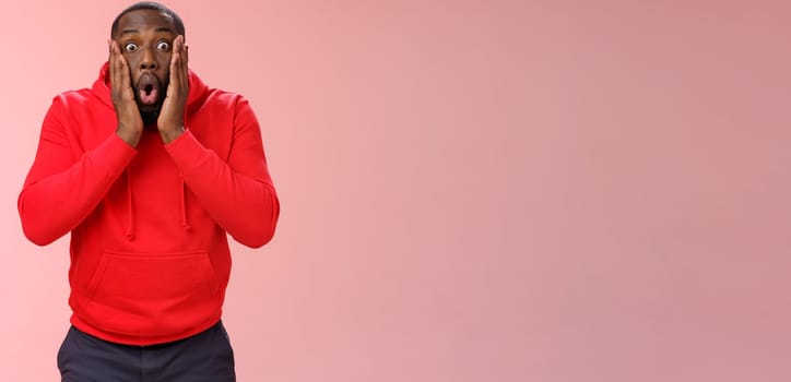 Wow incredible. Portrait impressed surprised african-american bearded guy in red hoodie folding lips bending widen eyes shocked see incredible offer standing amused excited, pink background.