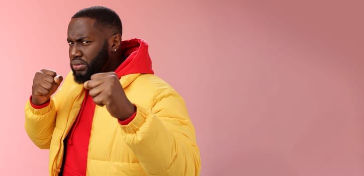 Lifestyle. Serious-looking angry irritated young black bearded man pissed rude person attidude raise fists frowning grimacing anger furious feel punch face standing boxing pose wanna fight pink background.