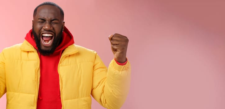 Handsome african-american man encouraging himself put will effort clenched arms yelling close eyes raise hands boost confidence, standing pink background express rage release emotions.