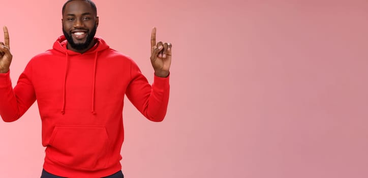 Devious cute african-american bearded guy in red hoodie smiling mysterious know exactly what you want pointing raised index fingers up grinning show perfect copy space promo, pink background.