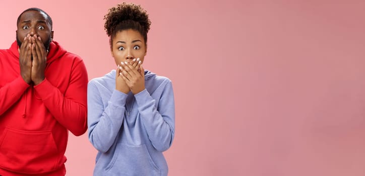 Two shocked african-american man woman widen eyes concerned terribly sorry press palms mouth gasping witness disaster hear sad bad news, standing worried pink background sympathizing friend.