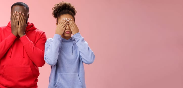 Two african-american man woman standing pink background hide faces close eyes palms tired looking lies upset waiting sign command see, playing hide-n-seek, unwilling spot personal problems.