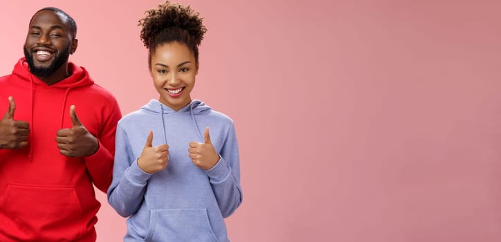 Best friends support your choice. Portrait proud satisfied good-looking african-american man woman show camera thumbs-up smiling broadly cheering liking awesome purchase, standing pink background.